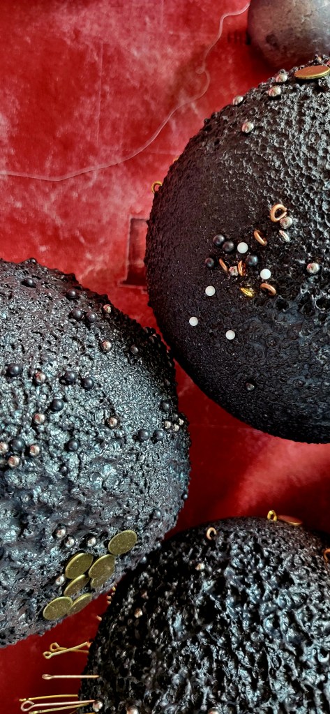 Roxana Donaldson, Safety First art installation 16, Assemblage art black spheres, detail, 2025. Black porous sphere with pins, wires and nails on a white wall in official Safety First the Aftermath exhibtion, Bucharest, Galeria Calea Victoriei 91-93, 2025.