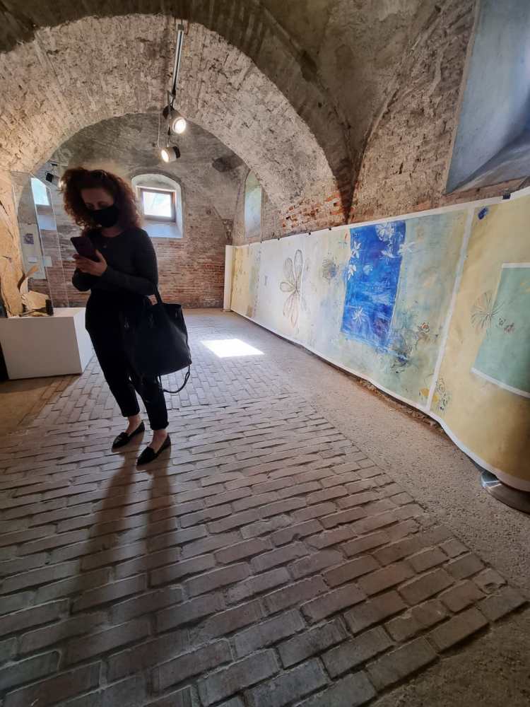 Roxana Donaldson standing in Fragmentum exhibition in front of monumental layered composition, painting fine art, 1.5x10m mixed media-paper, 2021