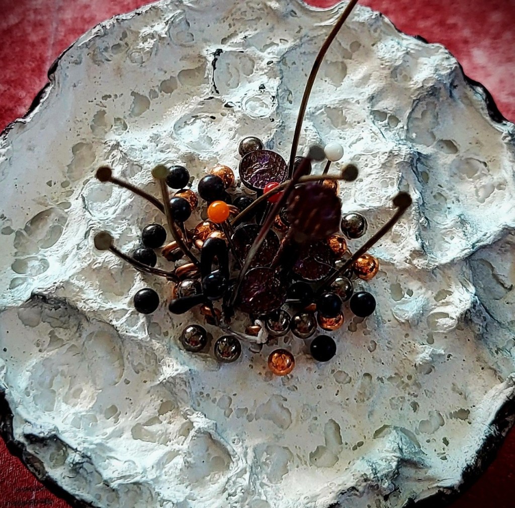 Roxana Donaldson, Safety First art installation 13, Assemblage art black spheres, detail, 2025. Black porous sphere with pins, wires and nails on a white wall in official Safety First the Aftermath exhibtion, Bucharest, Galeria Calea Victoriei 91-93, 2025.