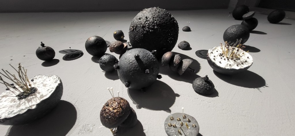 Roxana Donaldson, Saftey First art installation, Assemblage art black spheres, detail, 2025. Black porous sphere with pins, wires and nails on a white wall in official Safety First the Aftermath exhibtion, Bucharest, Galeria Calea Victoriei 91-93, 2025.