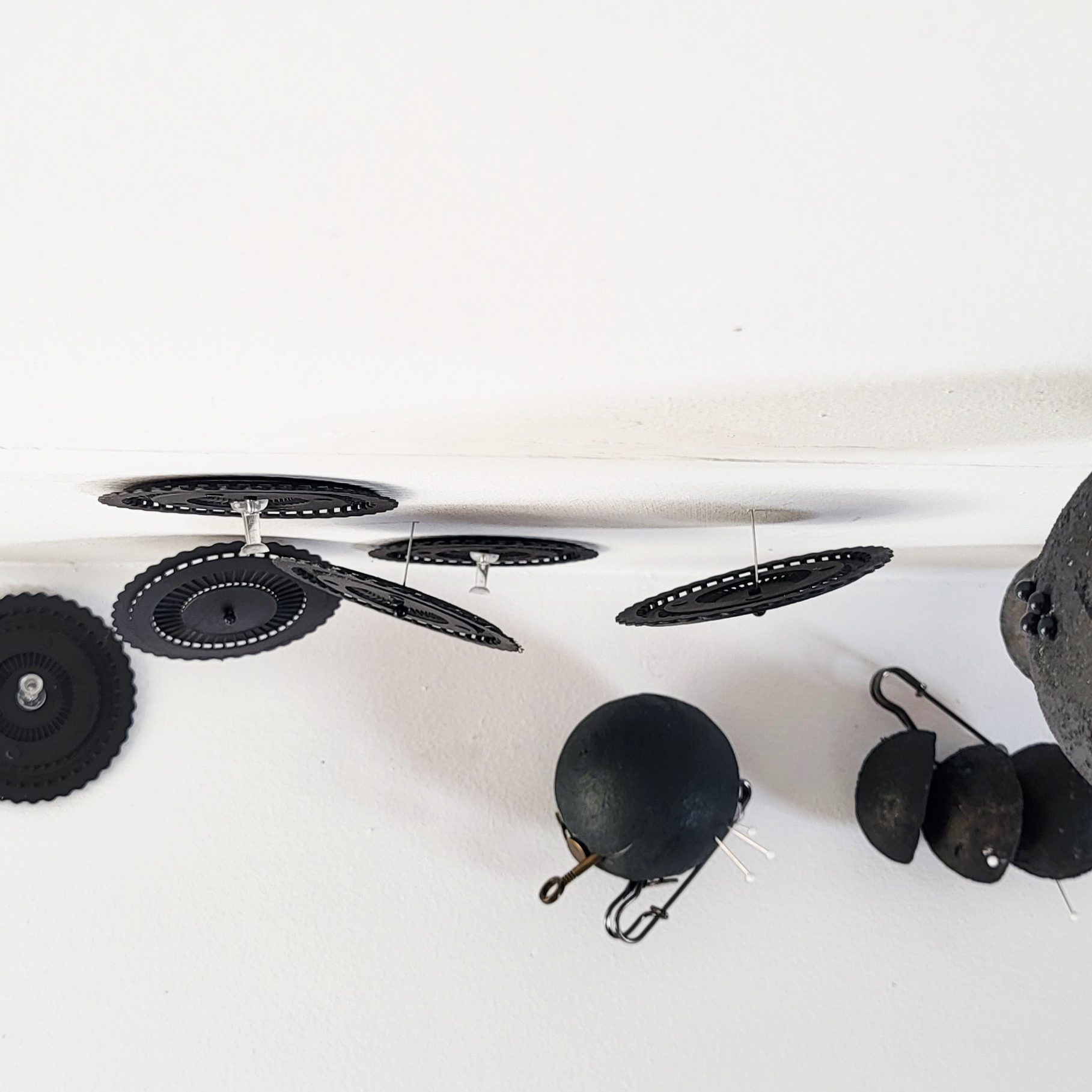 Roxana Donaldson, Saftey First art installation 1, Assemblage art black spheres, detail, 2025. Black porous sphere with pins, wires and nails on a white wall in official Safety First the Aftermath exhibtion, Bucharest, Galeria Calea Victoriei 91-93, 2025.