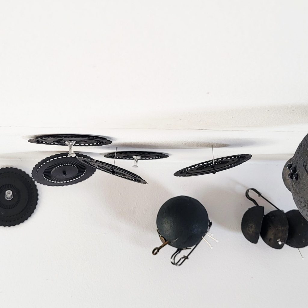 Roxana Donaldson, Saftey First art installation, Assemblage art black spheres, detail, 2025. Black porous sphere with pins, wires and nails on a white wall in official Safety First the Aftermath exhibtion, Bucharest, Galeria Calea Victoriei 91-93, 2025.