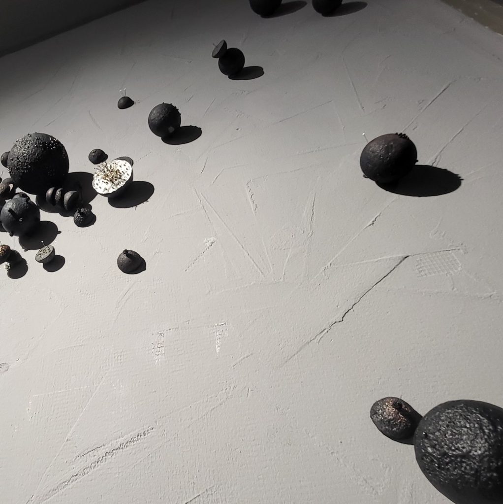 Roxana Donaldson, Saftey First art installation, Assemblage art black spheres, detail, 2025. Black porous sphere with pins, wires and nails on a white wall in official Safety First the Aftermath exhibtion, Bucharest, Galeria Calea Victoriei 91-93, 2025.